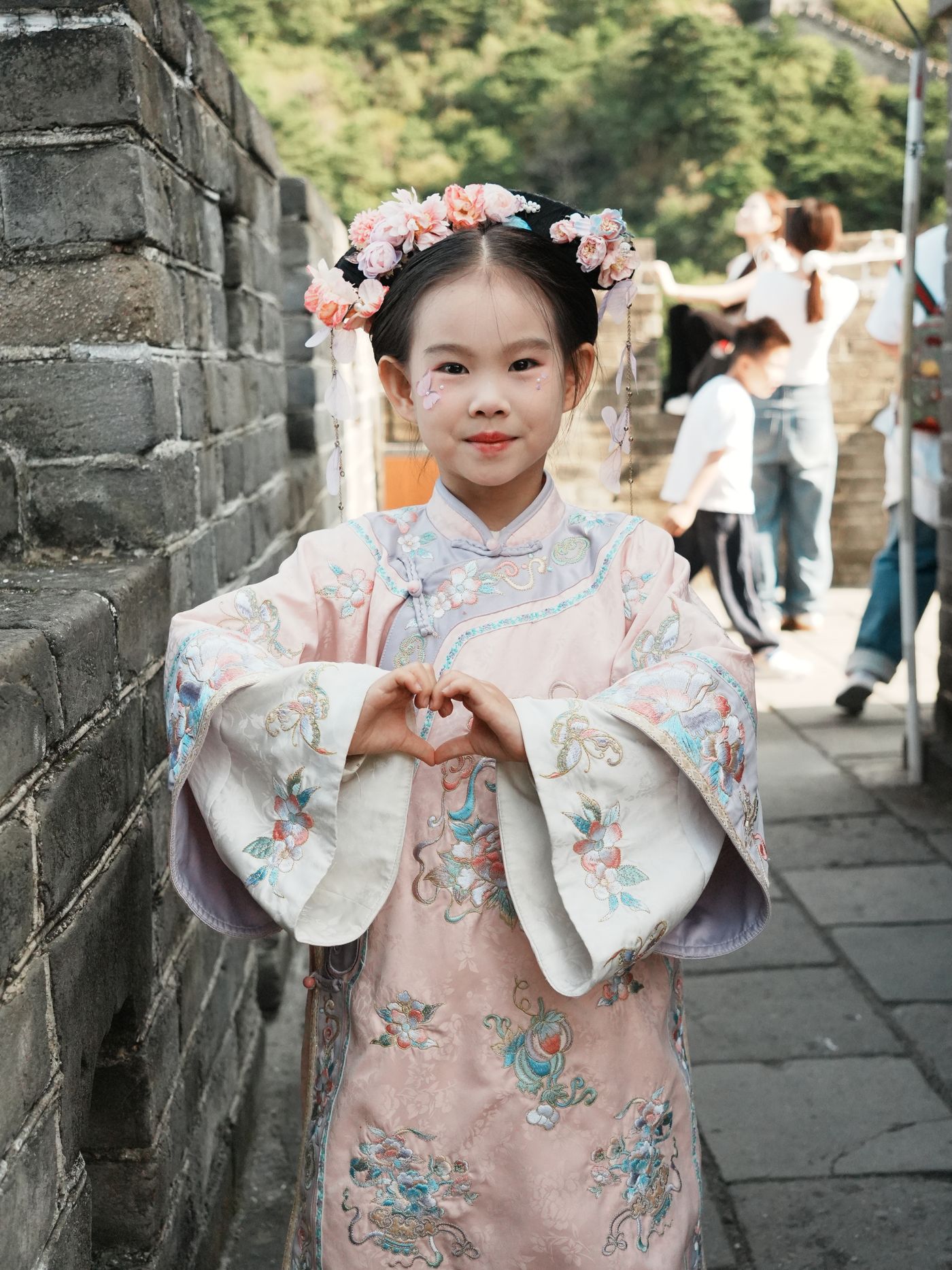Young girl in traditional pink Hanfu with floral headdress smiling on the Great Wall of China