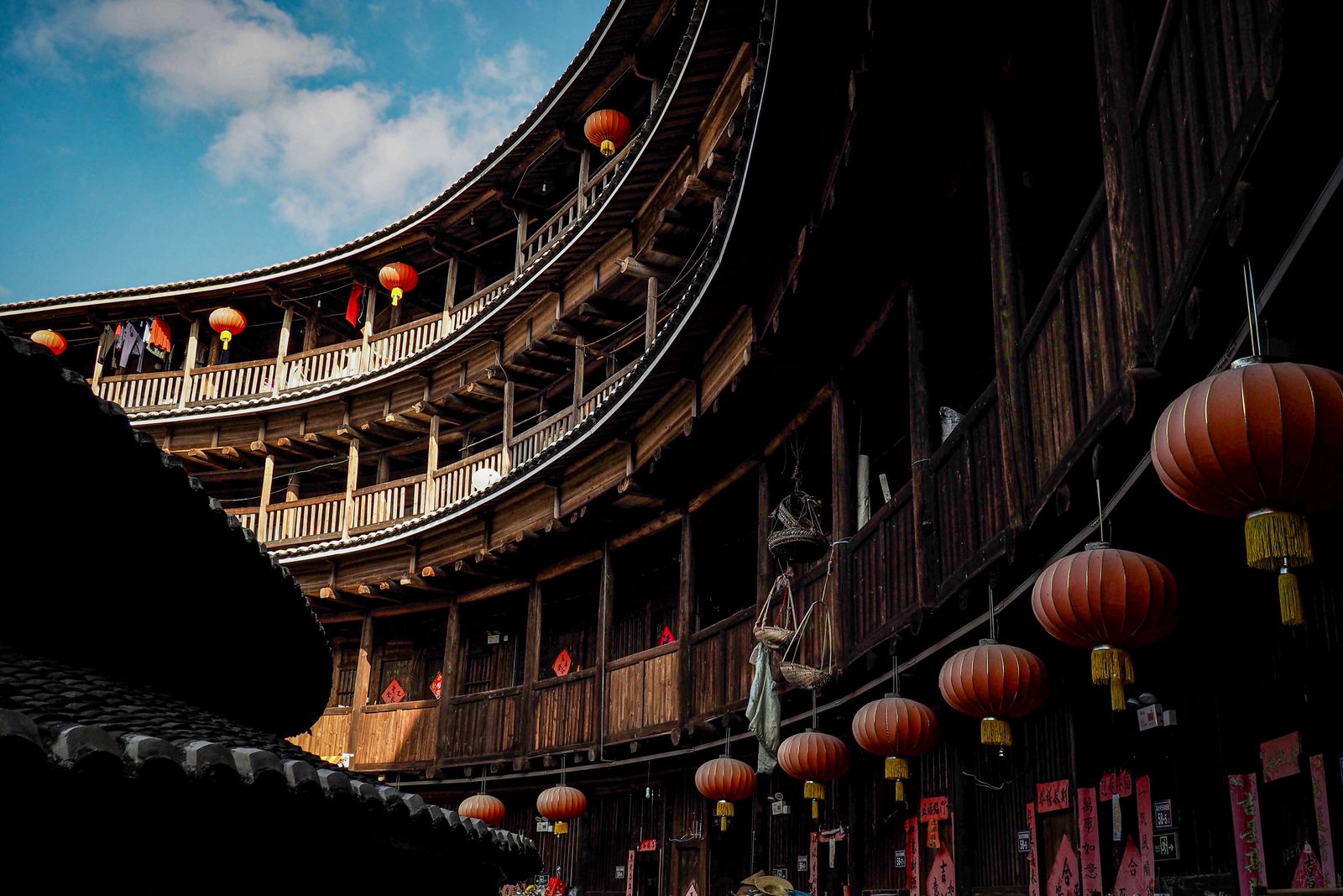 Historic Chinese Tulou roundhouse with red lanterns under a blue sky